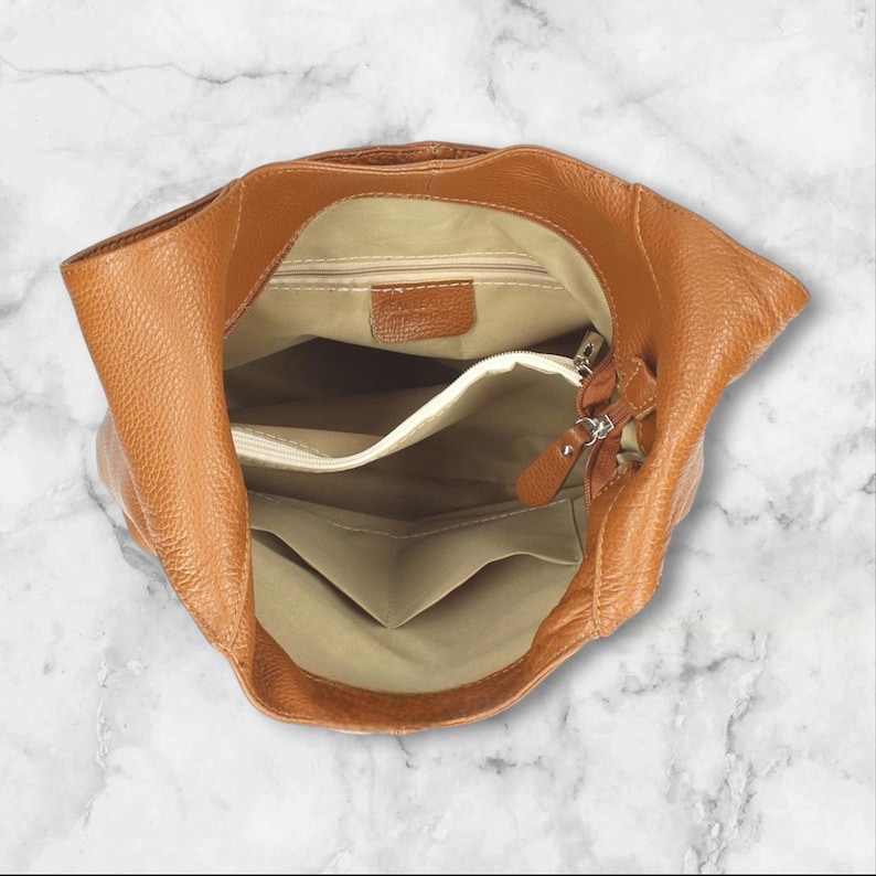 May include: Inside view of a brown leather handbag with a zip closure. The bag has a beige lining and multiple pockets.