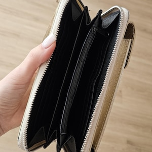May include: Open, gold-colored wallet with a zipper closure. The interior is black with multiple compartments and a zippered pocket. The wallet is held open, showcasing its storage capacity and design.