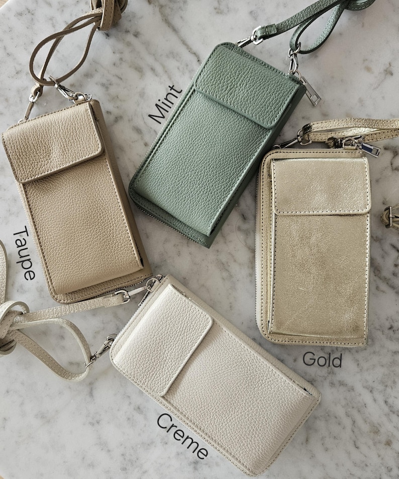 May include: Four leather crossbody phone bags in taupe, mint, gold, and creme. Each bag has a flap closure, a zipper, and a long strap. The bags are displayed on a marble surface.