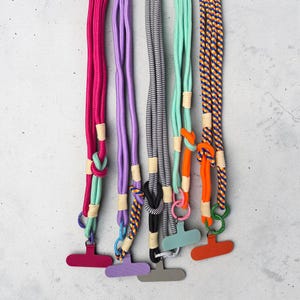 Puede incluir: Un juego de tres tazas de cerámica con un esmalte moteado de color crema. Cada taza presenta un diseño pintado a mano diferente: una hoja azul y verde, una flor amarilla y una baya roja. Las tazas tienen una forma simple y redondeada.