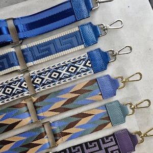 Op de afbeelding: Een verzameling kleurrijke geweven banden met verschillende patronen. De banden zijn gemaakt van katoen en hebben een verscheidenheid aan kleuren, waaronder blauw, wit, bruin en zwart. De banden zijn perfect om elke tas of handtas een vleugje stijl te geven.