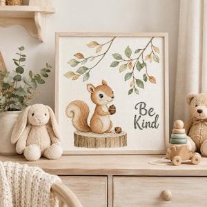 May include: A square framed cross-stitch art piece featuring a light brown squirrel sitting on a tree stump, holding an acorn. Above the squirrel are green and orange leaves on branches. The text Be Kind is printed in dark gray on the right side.
