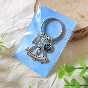 Può includere: Un portachiavi in metallo color argento con un anello circolare, un ciondolo a forma di lettera U, un piccolo ciondolo rotondo con superficie blu scuro glitterata e un ciondolo a forma di UFO con un alieno e la scritta "I WANT TO BELIEVE".
