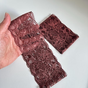 May include: Two pieces of burgundy lace fabric with a floral pattern. One piece is folded, and the other is rectangular. The lace has a scalloped edge and is displayed on a white background.