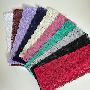 May include: A collection of lace fabric strips in various colors, including white, brown, lavender, navy, cream, pink, green, gray, black, and red. The lace has a detailed floral pattern.