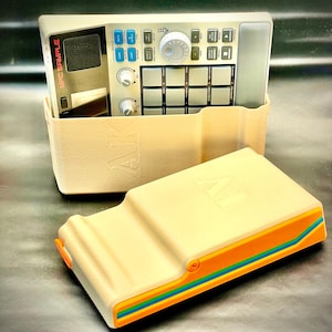 May include: A beige MPC Sample music production device with a matching case. The device has various buttons, knobs, and a screen. The case has a colorful stripe design with orange, blue, and green accents. The text "MPC SAMPLE" is visible.