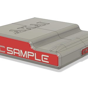 May include: A gray electronic device with the word "AKAI" on top and "MPC SAMPLE" on a red panel. The device has a rectangular shape with a curved top and a small red button on the side.