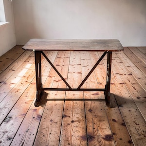 May include: A rustic wooden table with a rectangular top and dark brown metal legs. The table has a distressed finish, showcasing the natural wood grain. The legs feature a distinctive V-shaped support structure. The table is approximately 36 inches long.