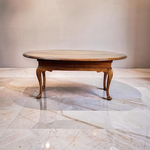 May include: Oval-shaped wooden coffee table with a dark brown finish. The table has a smooth, polished surface and curved legs. The table is approximately 48 inches long and 30 inches wide.