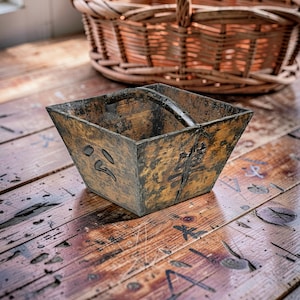 May include: A weathered, square wooden basket with a dark handle and Japanese characters etched on the side. The basket sits on a distressed wooden surface, with a woven basket in the background.