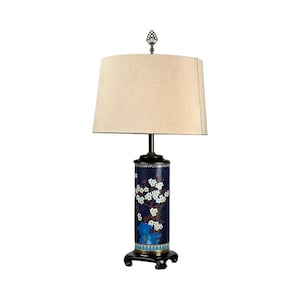 May include: A decorative table lamp with a cylindrical base featuring a dark blue floral design. The lamp has a beige lampshade and a dark bronze-colored base and accents. The lamp is on a black, ornate base.