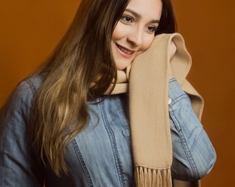 May include: A woman wearing a blue denim jacket with a brown scarf around her neck. She is smiling and looking to the side.