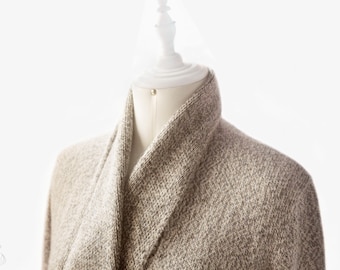 May include: A beige knitted cardigan with a shawl collar. The cardigan is draped over a white mannequin.