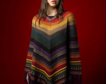Può includere: Una donna indossa un poncho a righe colorate con frange. Il poncho ha un collo a V ed è fatto di un tessuto morbido e lavorato a maglia.