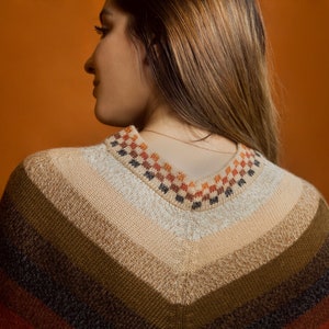 Pu&ograve; includere: Un poncho lavorato a maglia con scollo a V. Il poncho presenta una sfumatura di colore, che va dal beige chiaro al marrone scuro e al rosso. Lo scollo &egrave; decorato con un motivo geometrico arancione, marrone e nero.
