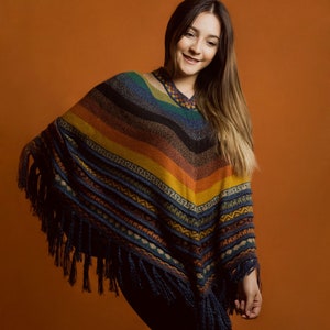 Pu&ograve; includere: Un poncho colorato con scollo a V e frange. Il poncho presenta strisce blu, verdi, arancioni e gialle. L'indumento ha un motivo geometrico nella parte inferiore ed &egrave; indossato da una persona.