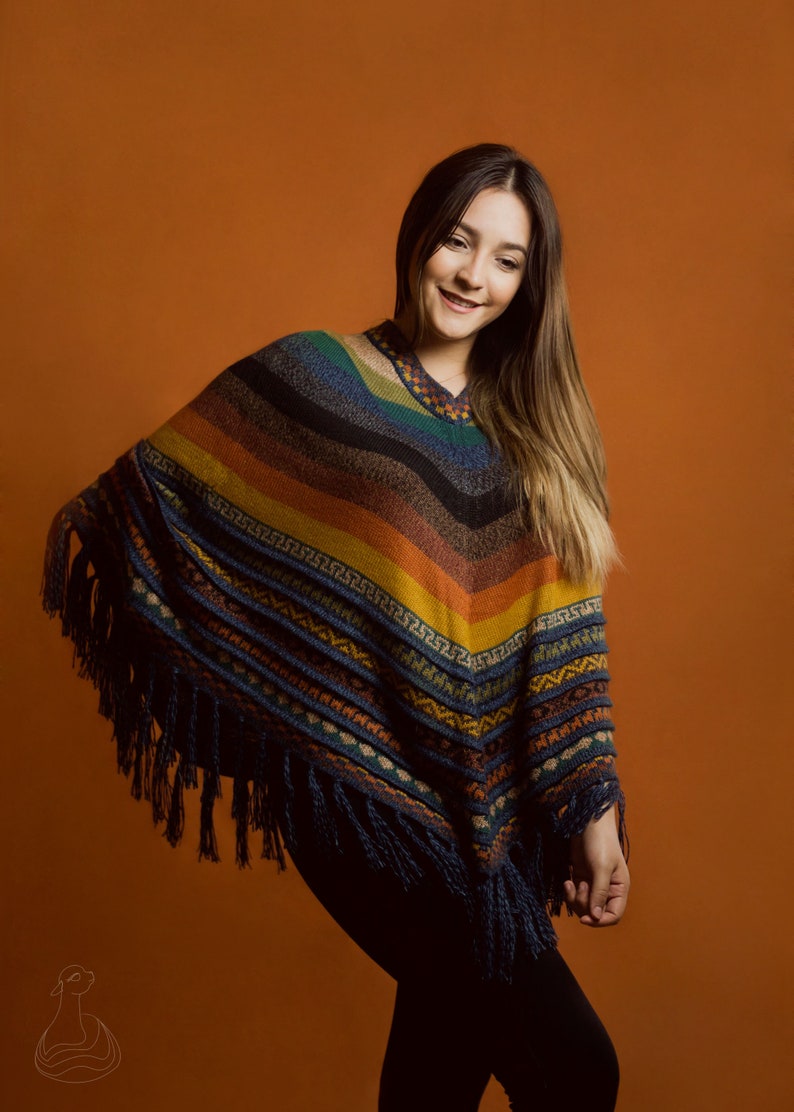 Pu&ograve; includere: Un poncho colorato con scollo a V e frange. Il poncho presenta strisce blu, verdi, arancioni e gialle. L'indumento ha un motivo geometrico nella parte inferiore ed &egrave; indossato da una persona.