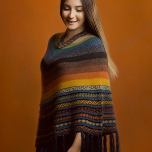 Pu&ograve; includere: Un poncho colorato e fantasia con scollo a V e frange. Il poncho presenta strisce orizzontali nei toni del blu, marrone, giallo e arancione. Il design include motivi geometrici ed &egrave; realizzato in un materiale morbido e tessuto.