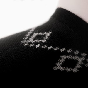 以下が含まれることがあります： 白い幾何学模様の黒い靴下。靴下は柔らかく快適な素材で作られています。