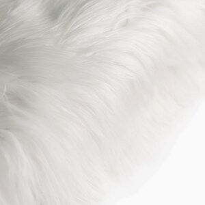 May include: White faux fur fabric with a soft, fluffy texture. The fur is arranged in a flowing, wave-like pattern.