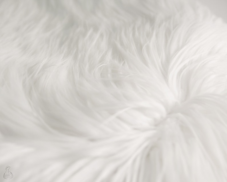 May include: Close-up of a white faux fur fabric. The fur is soft and fluffy, with a subtle swirl pattern.