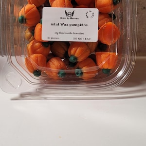 Könnte beinhalten: Ein durchsichtiger Plastikbehälter gefüllt mit 40 kleinen orangefarbenen Wachs-Kürbissen mit grünen Stielen. Der Behälter trägt ein Etikett mit der Aufschrift "Scent by Heaven mini Wax pumpkins soy blend candle decoration DO NOT EAT!"