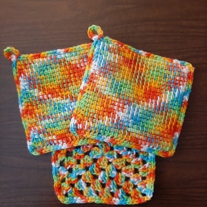 May include: Three colourful, handmade crochet pot holders. Two are square with a loop for hanging, featuring a woven pattern in shades of red, orange, yellow, green, blue, and white. The third has an open, lacy design in similar colours.