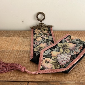 Könnte beinhalten: Zwei Vintage-Wandteppiche mit Blumen- und Fruchtdesigns. Der schwarze Stoff ist mit rosa Zierleisten versehen. Ein Aufhänger hat eine dekorative Metallspitze und der andere eine rosa Quaste.