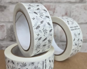May include: Three rolls of decorative tape with a white background and a repeating pattern of black leaves and floral elements. The tape has the text "I'M ECO-FRIENDLY PLEASE RECYCLE ME" printed on the side.