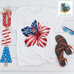 May include: White t-shirt featuring a large floral design with a patriotic theme. The flower design incorporates the American flag's stars and stripes. The text "DO NOT COPY" is visible on the flower. The shirt is paired with sandals and sunglasses.