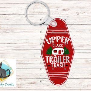 May include: Red keychain with the words "UPPER CLASS TRAILER TRASH" in white, with a white camper and green trees. The keychain has a silver ring and a white plastic attachment.