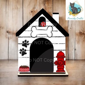 Könnte beinhalten: Ein weißes Hundehaus aus Holz mit schwarzen Verzierungen. Das Haus hat einen roten Ball, einen Knochen, Pfotenabdrücke und einen roten Hydranten. Das Haus steht auf einem Holzsockel.