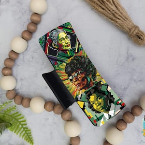 May include: A phone case with a colorful design featuring portraits of three women. The case is black and has a raised edge around the camera lens.