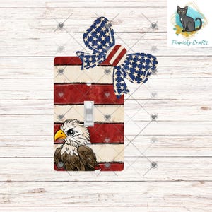 Könnte beinhalten: Eine dekorative Lichtschalterabdeckung mit einem Design der amerikanischen Flagge, mit roten und weißen Streifen und einer blauen Schleife mit weißen Sternen. Eine Illustration eines Weißkopfseeadlers befindet sich unten. Der Schalter ist weiß.