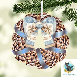 Op de afbeelding: Een kerstornament in de vorm van een krans, met een ontwerp van dennenappels en een blauwe strik met sneeuwvlokken en sjaal details. Het ornament hangt aan een wit lint en is geschikt voor feestelijke decoratie.