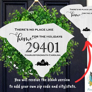 May include: A white wooden sign shaped like the state of South Carolina with the text "There's no place like home for the holidays" and a zip code "29401" and the city and state "Charleston, South Carolina". The sign is surrounded by a green wreath. The text "You will receive the blank version to add your own zip code and city/state." is below the sign.