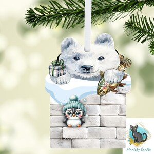Könnte beinhalten: Weihnachtsschmuck mit einem Eisbären, der ein Geschenk und einen Fisch hält. Darunter sitzt ein Pinguin mit blauer Mütze und Brille auf einer Ziegelmauer. Der Schmuck hat ein weißes Band zum Aufhängen.