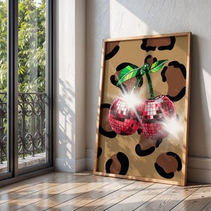 May include: A framed art print featuring two cherries designed as disco balls. The cherries are red with reflective squares, green leaves, and a brown stem. The background is tan with brown leopard spots.