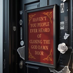 Könnte beinhalten: Ein gerahmtes Schild mit dem Text "HAVEN'T YOU PEOPLE EVER HEARD OF CLOSING THE GOD DAMN DOOR" in goldener Schrift auf rotem Hintergrund. Der Rahmen ist schwarz, und das Schild ist an einer schwarzen Tür angebracht.