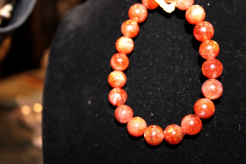 May include: A red sunstone beaded bracelet with a gold clasp. The beads are round and have a sparkly finish.