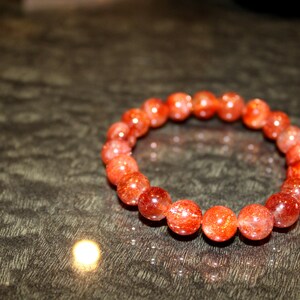 May include: A red sunstone bracelet with round beads. The bracelet is made of natural stones and has a polished finish.