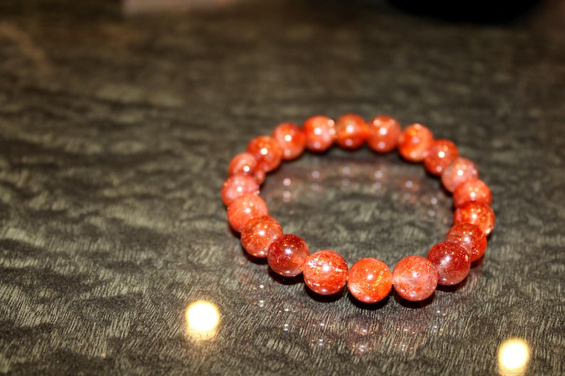 May include: A red sunstone bracelet with round beads. The bracelet is made of natural stones and has a polished finish.