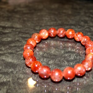 May include: A red sunstone beaded bracelet with a shiny, sparkly finish.