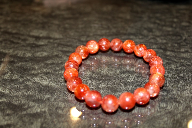 May include: A red sunstone beaded bracelet with a shiny, sparkly finish.