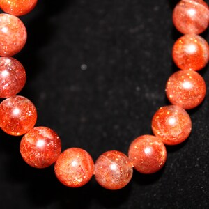 May include: A bracelet made of round, orange sunstone beads. The beads are polished and have a sparkly, iridescent finish.
