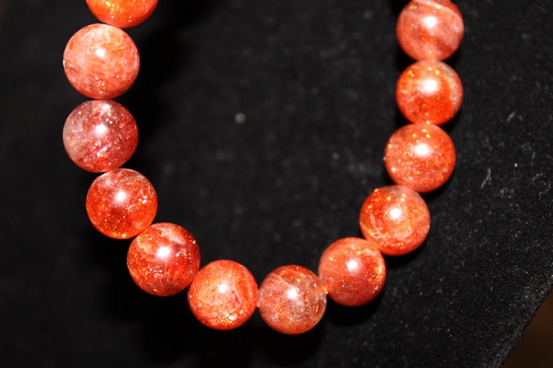 May include: A bracelet made of round, orange sunstone beads. The beads are polished and have a sparkly, iridescent finish.