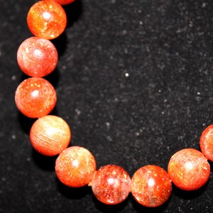 May include: A bracelet made of orange sunstone beads. The beads are round and have a smooth, polished finish.