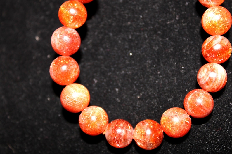 May include: A bracelet made of orange sunstone beads. The beads are round and have a smooth, polished finish.