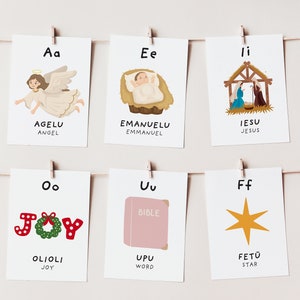 May include: Six illustrated flashcards with the letters A, E, I, O, U, and F. Each card features a Christmas-themed image and the corresponding word in English and a foreign language. The words are Angel, Emmanuel, Jesus, Joy, Word, and Star.