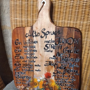 Puede incluir: Una tabla de cortar de madera con un diseño pintado con flores y el texto "Alter Spries", "Ein bißchen mehr FRIEDEN", "STREN Gute", "Neid", "mehr WAHRHEIT", "immer da", "Hilfe bei Gefahr", "Wir", "Kraft und nicht", "so zimper lich", "wahrend des", "LEBENS", "GRABER", "Vergebens".